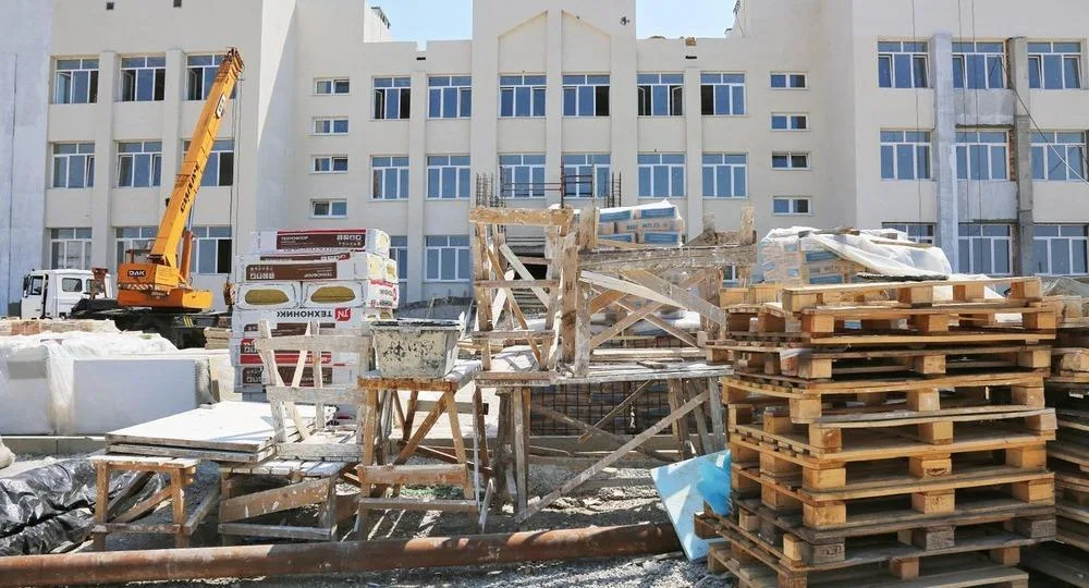 Строительные материалы в упаковке — утеплитель, поддоны — на площадке строящегося социального объекта рядом со строительным краном
